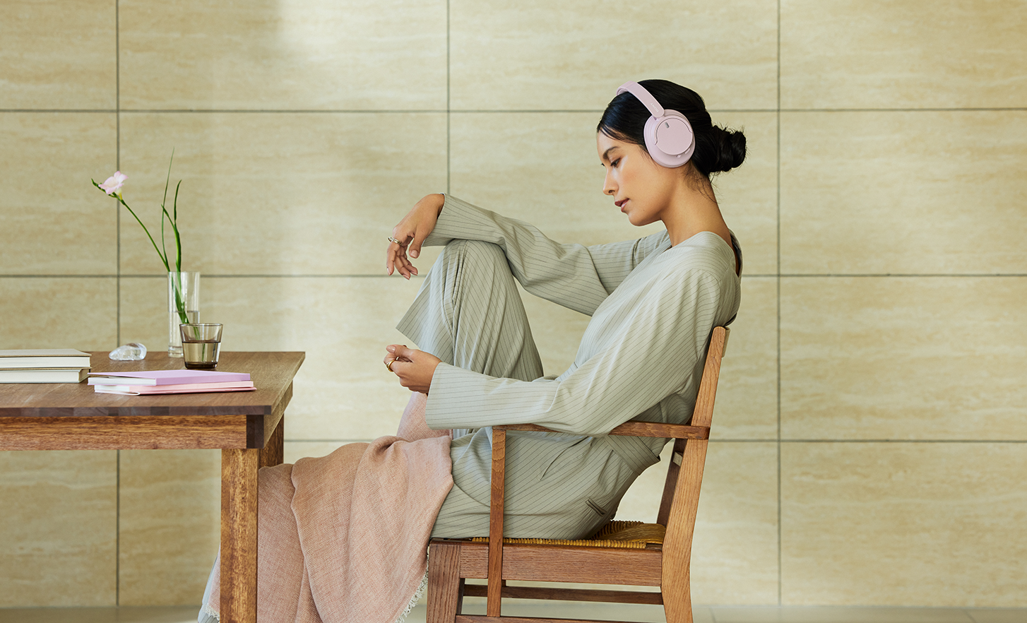 אדם מרכיב זוג אוזניות WH-CH720N ורודות שלSony ונרגע בחלל מינימליסטי.