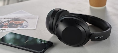 אוזניות WH-XB910N בצבע שחור, על שולחן, ליד כוס קפה וסמארטפון