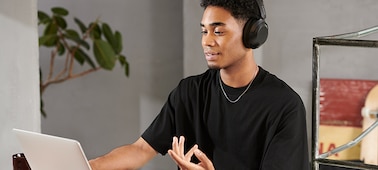 אדם יושב ליד שולחן ועובד על מחשב נייד כשהוא לובש אוזניות WH-XB910N