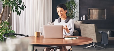 אישה יושבת ליד שולחן עם מחשב נייד ומרכיבה רמקול SRS-NS7 במהלך ניהול שיחה ללא שימוש בידיים