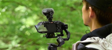 תמונת שימוש שמציגה משתמש מצלם ביד עם מיקרופון ומגן רוח מחוברים למצלמה