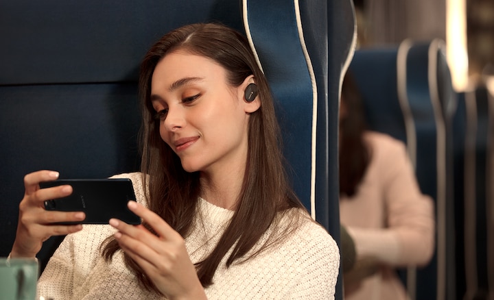 תמונה של אישה שמשתמשת באוזניות WF-1000XM3 כדי ליהנות מתוכן וידאו בטלפון החכם שלה.