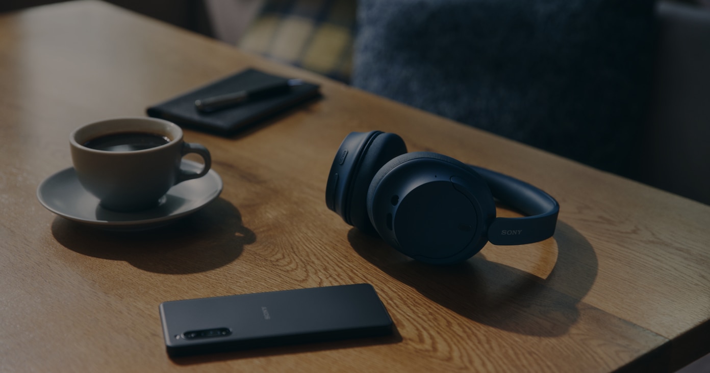 Image of a table with Sony Wireless headphones, a cup of coffee and a mobile phone on top