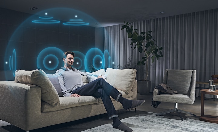 גבר יושב על ספה ונהנה מצליל מרחבי 360 באמצעות רמקול לביש SRS-NS7 ומשדר אלחוטי WLA-NS7