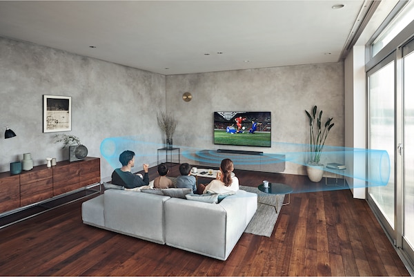 משפחה יושבת על ספה בסלון וצופה בטלוויזיה עם מקרן קול HT-A7000 על גבי ארונית שיש ו-Immersive AE כבוי