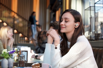 תמונה של אישה בבית קפה שנהנית מהשימוש באוזניות WF-1000XM3