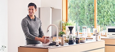 Man at a sink washing dishes while wearing the SRS-NB10 Wireless Neckband Speaker in black
