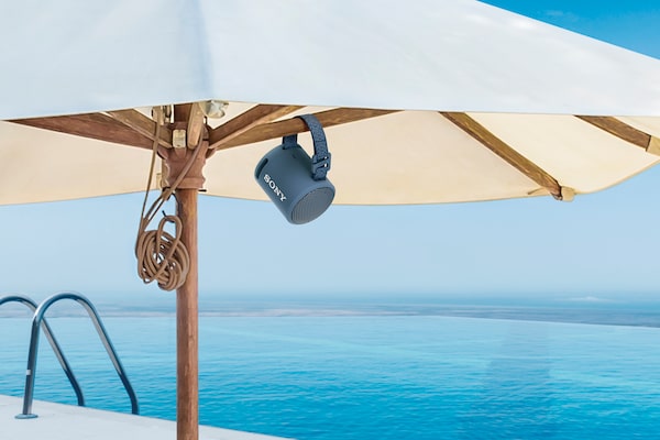 Image of the XB13 EXTRA BASS(TM) Portable Wireless Speaker attached to a parasol on a tropical beach.