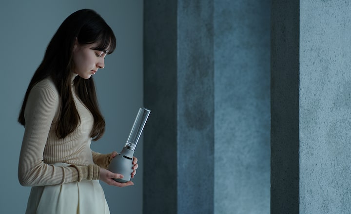 אישה צעירה מחזיקה רמקול זכוכית מסוג Sony LSPX-S3 כדי להראות כמה הוא נייד.