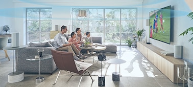 משפחה על ספה צופה בטלוויזיה עם מערכת קולנוע ביתי HT-A9 מונת על שידה מעץ ו-Immersive AE פועל וכיפה של גלי קול בחדר.