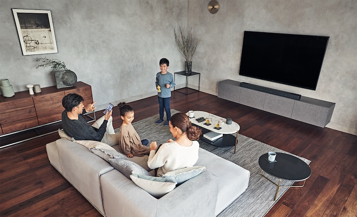 משפחה שנהנית ממוזיקה בסלון עם טלוויזיה ומקרן הקול HT-A7000 על ארונית שיש