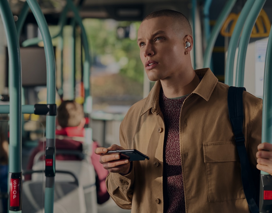 Image of a person holding a mobile phone on a bus while listening to music with a Sony Truly Wireless earbuds