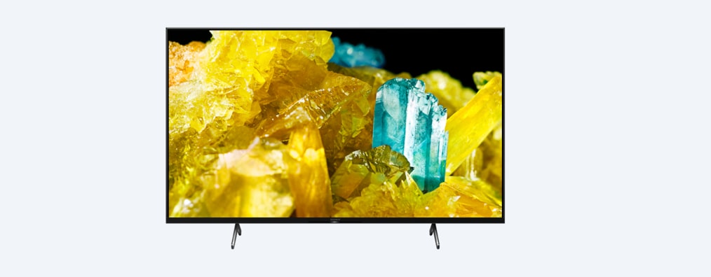 מבט מלפנים על טלוויזיית BRAVIA מסדרת X90S/P עם מעמד וצילום מסך של גבישים בצבעי צהוב וטורקיז
