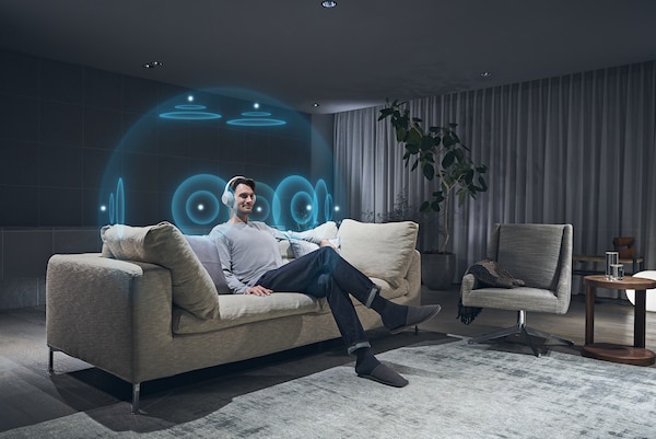 גבר יושב על ספה, מרכיב אוזניות ונהנה מצליל מרחבי ב-360 מעלות