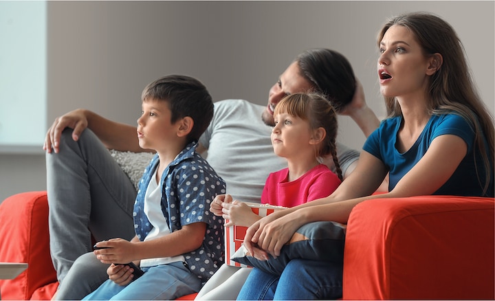 גבר ואישה עם שני ילדים יושבים על ספה וצופים בטלוויזיה