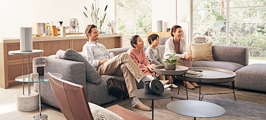 משפחה יושבת על ספה וצופה בטלוויזיה עם רמקולים סביב החדר שיוצרים חוויה סוחפת