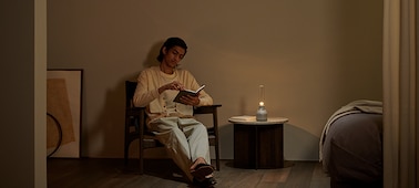 רמקול זכוכית מסוג Sony LSPX-S3 על גבי שולחן ליד אדם שקורא, עם תאורה עדינה.