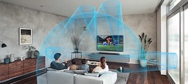 משפחה יושבת על ספה בסלון וצופה בטלוויזיה עם מקרן קול HT-A7000 על גבי ארונית שיש ו-Immersive AE פועל