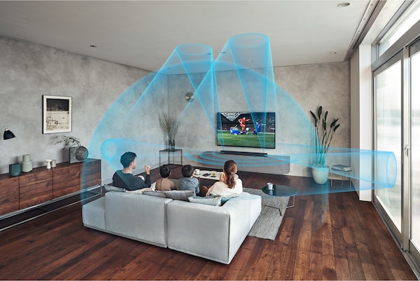 משפחה יושבת על ספה בסלון וצופה בטלוויזיה עם מקרן קול HT-A7000 על גבי ארונית שיש ו-Immersive AE פועל