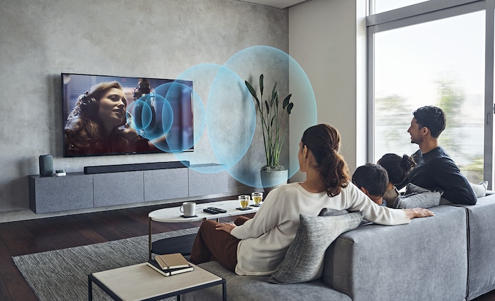 משפחה שצופה בטלוויזיה על הספה עם מקרן קול HT-A7000 על ארונית שיש