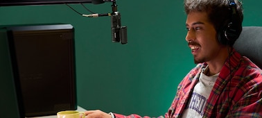 תמונת שימוש של גבר יושב מול צג של מחשב ומרכיב אוזניות שמחוברות על ידי כבל למיקרופון