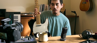תמונת שימוש של גבר מחזיק גיטרה ומדבר למיקרופון בקרבת מקום, בעודו מביט למצלמה עם מגבר מותקן
