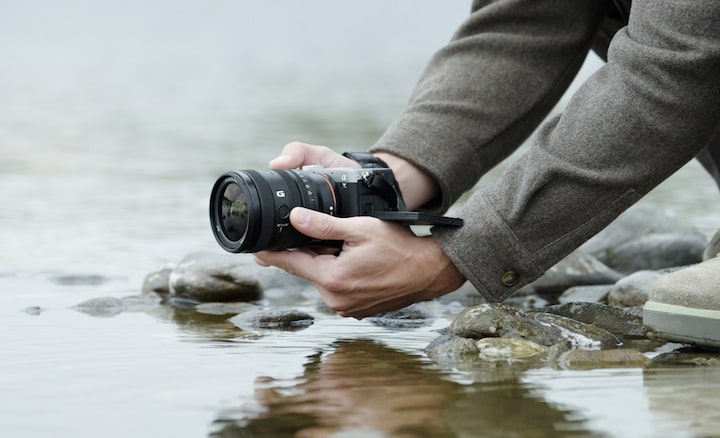 תמונת שימוש המציגה משתמש שמחזיק את α7CII עם עדשת FE 24-50mm F2.8 G ליד מי נהר. המשתמש מצלם מנקודה נמוכה