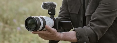 תמונת שימוש של גבר מצלם וידאו ביד עם עדשת טלפוטו מחוברת
