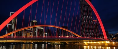 תמונת לילה של נוף עירוני, עם גשר מואר בצבע אדום בחזית