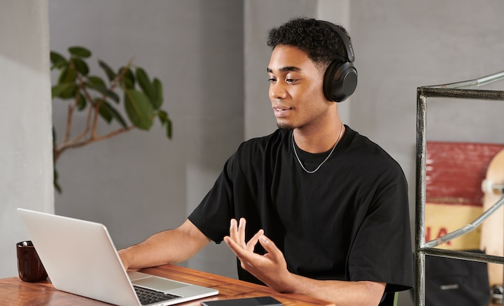 אדם יושב ליד שולחן ועובד על מחשב נייד כשהוא לובש אוזניות WH-XB910N